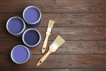 Cans with violet paints and brushes on wooden background, top view. Space for text