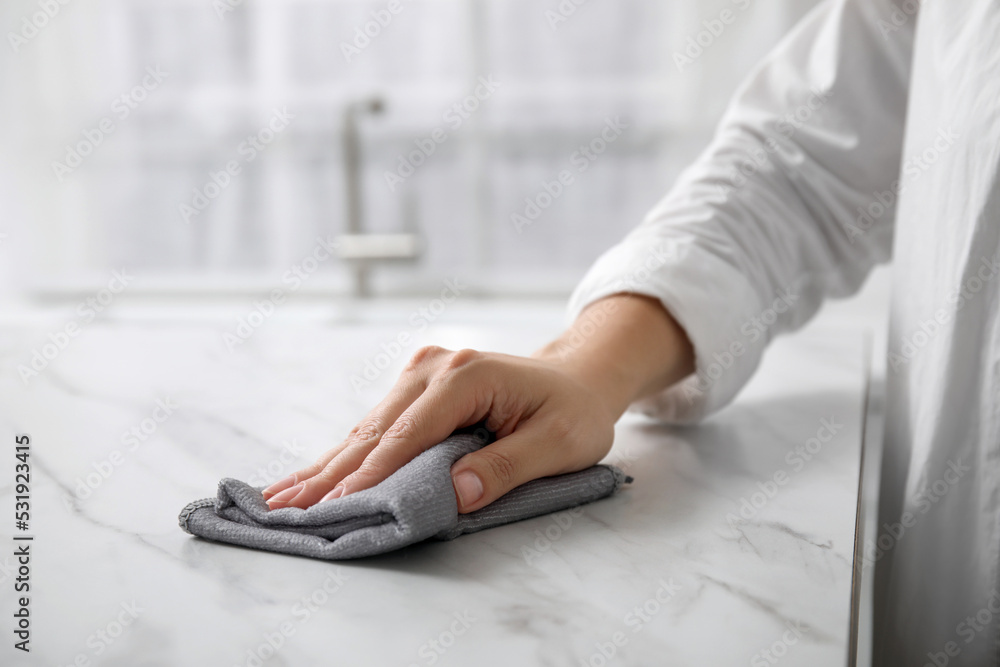 Sticker Woman wiping white marble table indoors, closeup