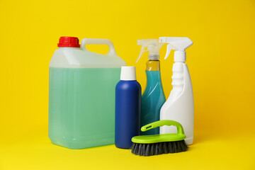 Bottles of detergents and brush on yellow background. Cleaning supplies