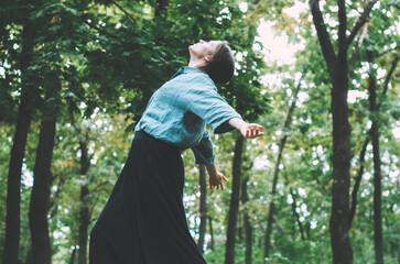 Side view of woman with arms outstretched, looking towards the sky, in the forest