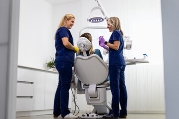 Female dentist with assistant working in dental clinic examining patient teeth.