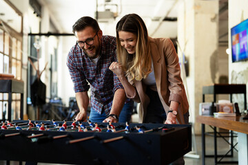 Fototapeta premium Colleagues having fun at work. Businessman and businesswoman playing table soccer