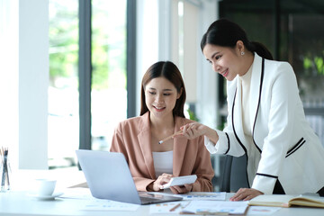 Two young Asian business woman talk, consult, discuss working with new startup project idea presentation analyze plan marketing and investment in the office.