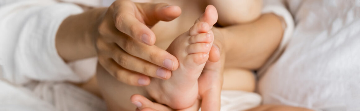 Cropped view of woman touching foot of infant daughter on blurred bed, banner.