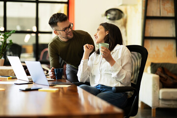 Colleagues laughing in office. Businesswoman and businessman drinking coffee
