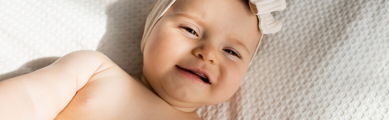 top view of infant girl in headband lying on bed and looking at camera, banner.