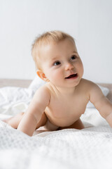Portrait of pleased baby girl looking away on white bedding at home.