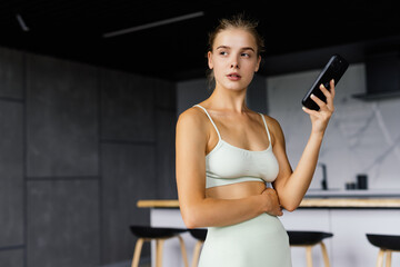 Fototapeta na wymiar Beautiful fit woman looking at smartphone, listening music and relaxing after training
