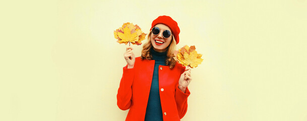 Autumn portrait of happy smiling young woman with yellow maple leaves wearing red french beret on gray background