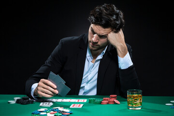 Depressed Frustrated Handsome Caucasian Brunet Young Pocker Player At Pocker Table With Chips And Cards While Drinking Alcohol.