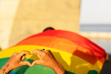 Hands making heart sign in front of rainbow flag