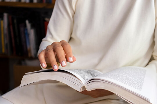Close up of woman hands holding book, with perfect beige manicure.