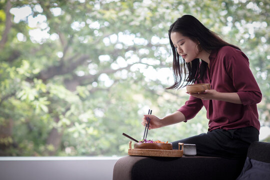 Young woman eating lunch with chopsticks at home