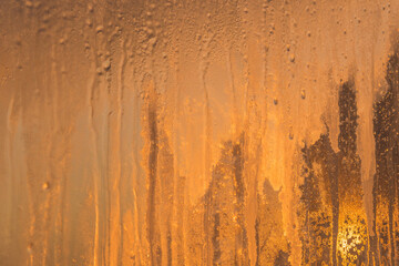 Frosty patterns on the glass, the dawn sun through the frost, yellow abstract winter background