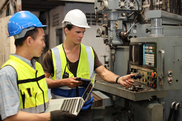 Technician engineer in protective uniform with hardhat standing and teaching apprentices or colleague worker to use computerized machine control at heavy industry manufacturing factory
