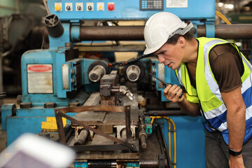 Technician engineer or worker man in protective suit standing and using walkie talkie radio while controlling or maintenance operation work lathe metal machine at heavy industry manufacturing factory