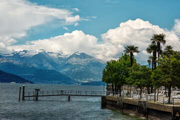 View of the pier on the lake Como, Italy, trees and recreation zone, with mountains Alps, sky and clouds in the background