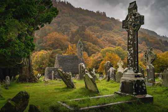 Medieval church ancient graves Celtic crosses in Glendalough Cemetery. Moody autumn forest, mountains in rain, storm sky in background Wicklow Ireland