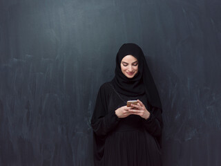 Young modern muslim business woman using smartphone wearing hijab clothes in front of black...