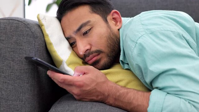 Bored, lonely and sad man with phone, social media and texting on home sofa lounge alone. Unhappy, depression and young guy waiting for mobile message and reading heartbreak notification in isolation