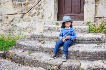 Little handsome baby boy sitting on ancient stone stairs and playing outdoor with straw hat in old city