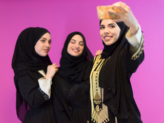 group of beautiful muslim women two of them in fashionable dress with hijab using mobile phone...