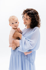 Positive woman in blue dress looking at infant daughter isolated on white.