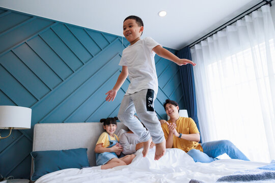 Boy Jump On Bed Show His Family Parent, Sister And Grandmom Cheerful Him Together At Bedroom.