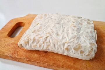 Tempe Mentah : Raw Tempeh, uncooked soybean cake from Indonesia in a plastic on a wooden cutting board isolated on white background