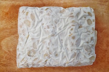 Tempe Mentah : Raw Tempeh, uncooked soybean cake from Indonesia in a plastic on a wooden cutting board isolated on white background