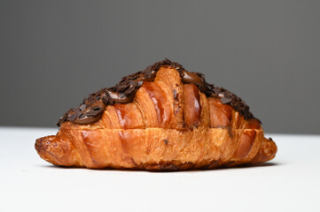 Close up of fresh croissant with chocolate sauce and chip. Bakery product. Side view