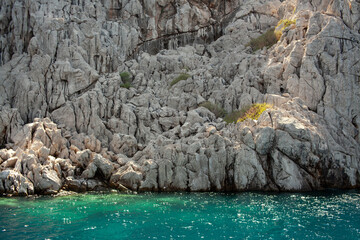 Aegean sea rocky shores with turquoise water. Lava stones and rocks. View from sea. Rock reflection...