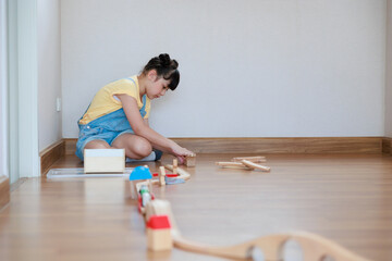 Asian cute girl playing wood block building rail way and road on the floor at home.