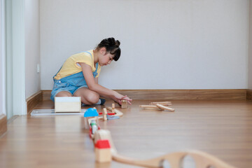 Asian cute girl playing wood block building rail way and road on the floor at home.