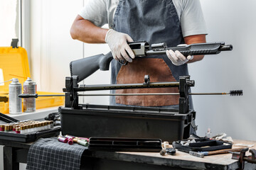 Close up of young man in apron disassembling a gun above the table - obrazy, fototapety, plakaty