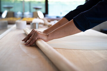 Close up of female hands working with rolling-pin for italian fresh pasta -  Female hands rolling  for fresh dough on the wooden table - concept of cooking and fresh homemade pasta