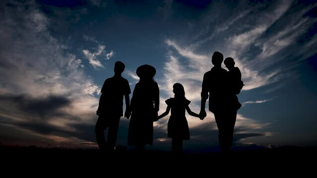 Happy family standing in the park during sunset. Silhouette of a young family. 4k video