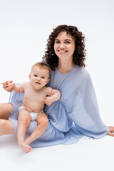 Happy woman holding hand of baby daughter and sitting on white background.