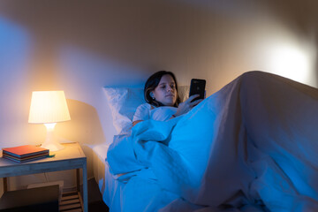 Girl looking her smart phone doom scrolling on bed in the middle of the night. Technology at bed...