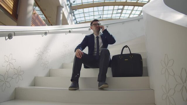 Entrepreneur sit on staircase in business center and talk on smartphone