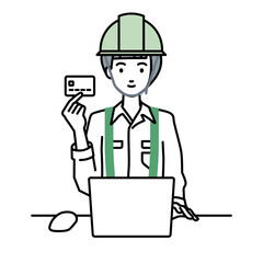 デスクで座ってPCを使いながらクレジットカードを手に持っている工事現場の女性