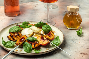 Burrata cheese and grilled peaches with basil and pine nuts, Two glasses of rose wine on a light...
