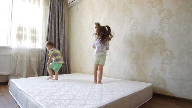 Happy funny little children, brother and sister, jumping on mattress. Cheerful cute active kids having fun playing during the repair.Leisure activity, lot of energy, hyperactive kid concept.Childhood.