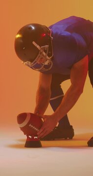 Vertical video of caucasian male american football player holding ball, with neon orange lighting