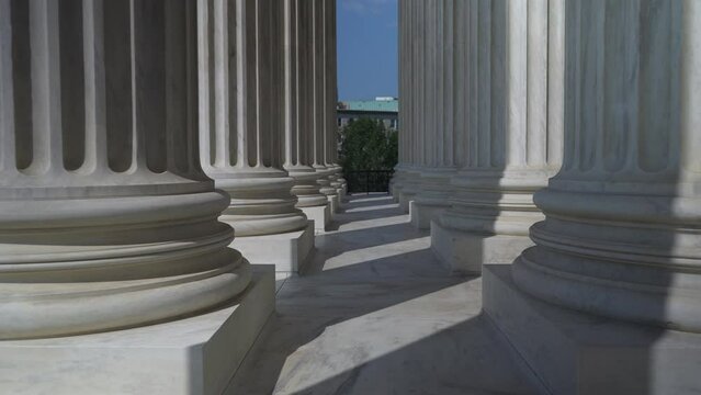 Slow motion pushing through very large towering columns in front of US Supreme Court building in Washington, DC showing judicial power over people and business.