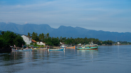 Fototapeta na wymiar Traditional fishing boats on the sea with blue sky and mountains in pantai pasir putih Situbondo 