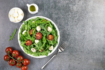 Green salad with arugula, cherry tomatoes, mozzarella cheese and olive oil on a gray background....