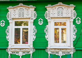 Old wooden windows with carved white architraves on green painted, sheathed with wooden slats...