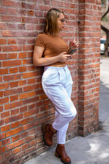 Young woman holding and using smartphone, waiting for a date, chatting on the street while waiting for her friends, taxi, ride