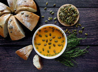 Pumpkin cream soup with pumpkin seeds and thyme, pumpkin bread. Wooden background, top view. 